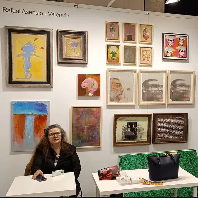 Una mujer se sienta a una mesa frente a una pared de pinturas de Rafael Asensio.