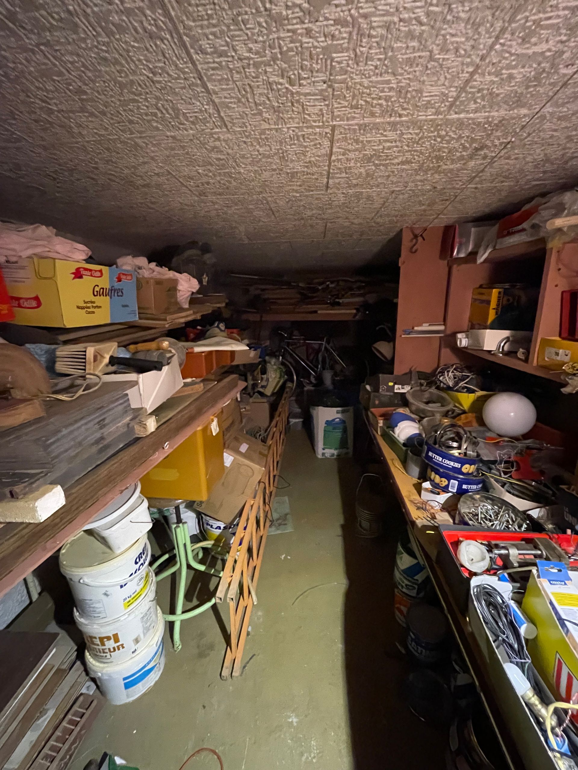 Des cartons d'ordures et de jouets s'entassent contre un mur de briques, à côté de poubelles vertes et grises.