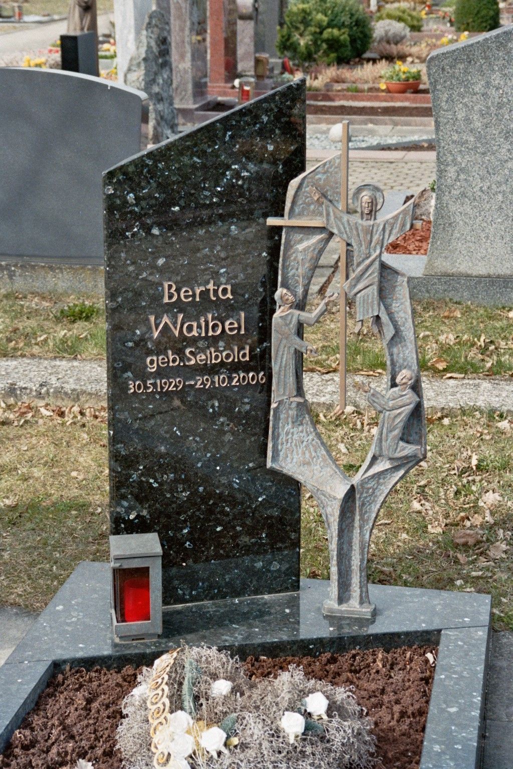 Ein Grabstein mit der Statue eines Mannes, der auf einem Friedhof ein Kreuz hält.