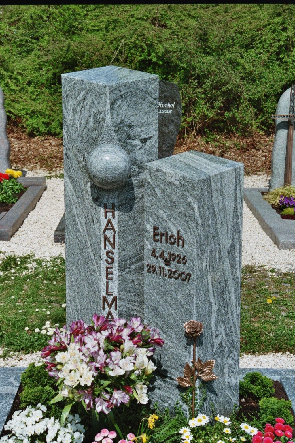 Ein Grabstein auf einem Friedhof mit Blumen davor.