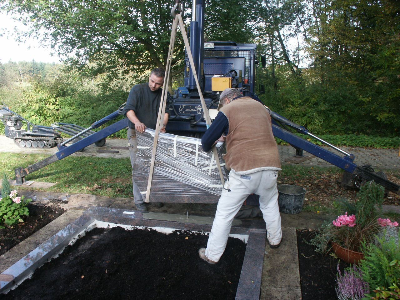 Zwei Männer arbeiten an einem Grab, im Hintergrund ein Kran