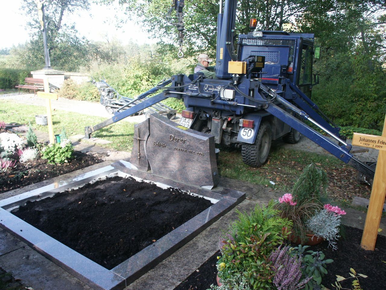 Ein blauer Lastwagen gräbt ein Grab auf einem Friedhof
