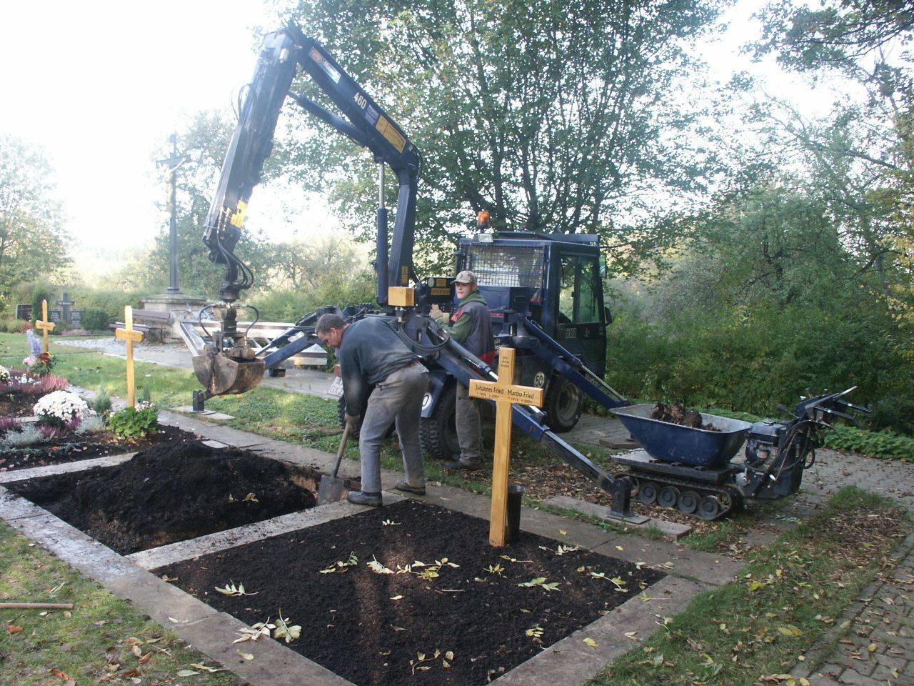 Ein Kran hebt ein Kreuz auf einen Friedhof