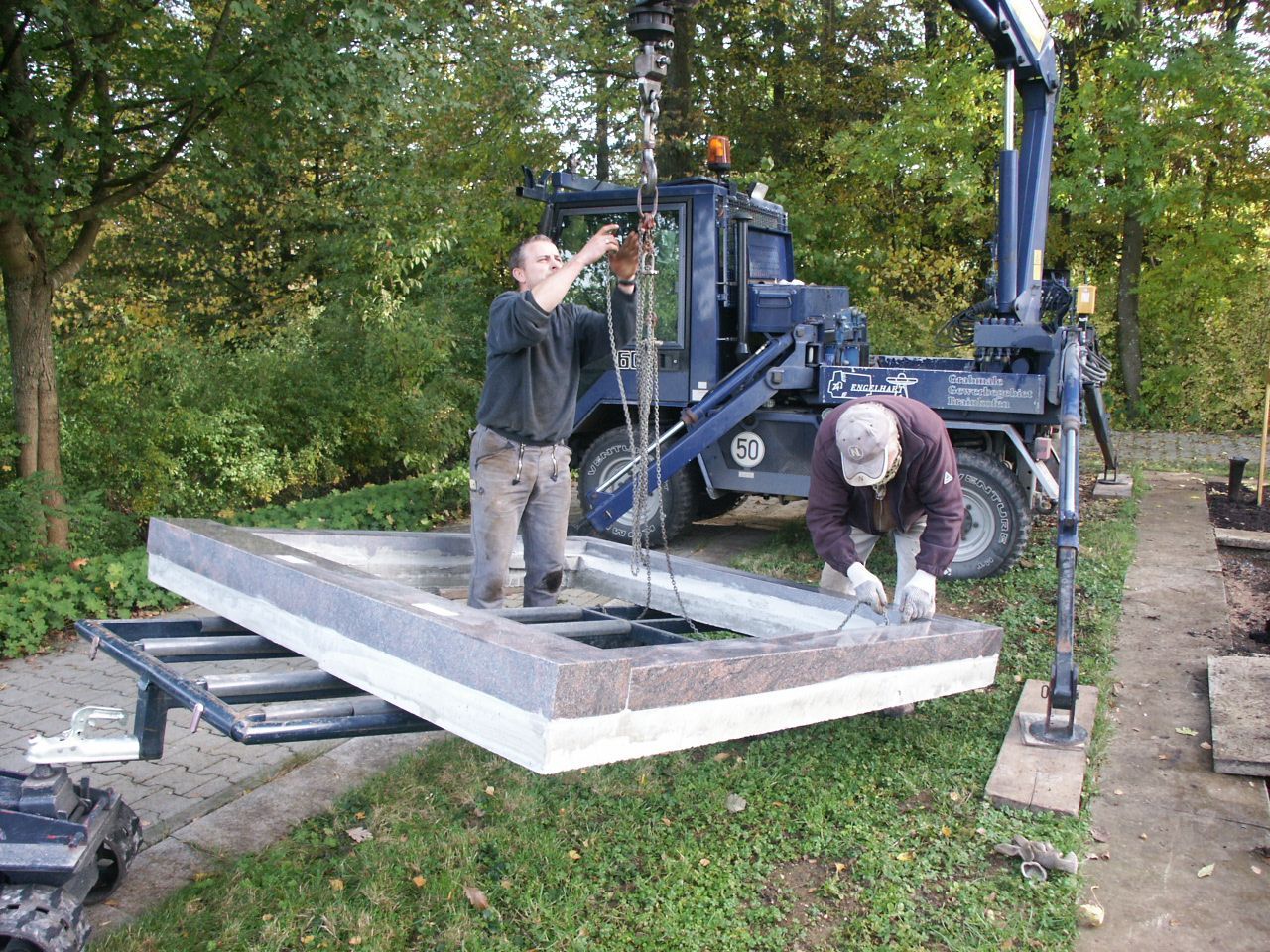 Zwei Männer arbeiten an einem großen Stück Beton, das von einem Kran angehoben wird.