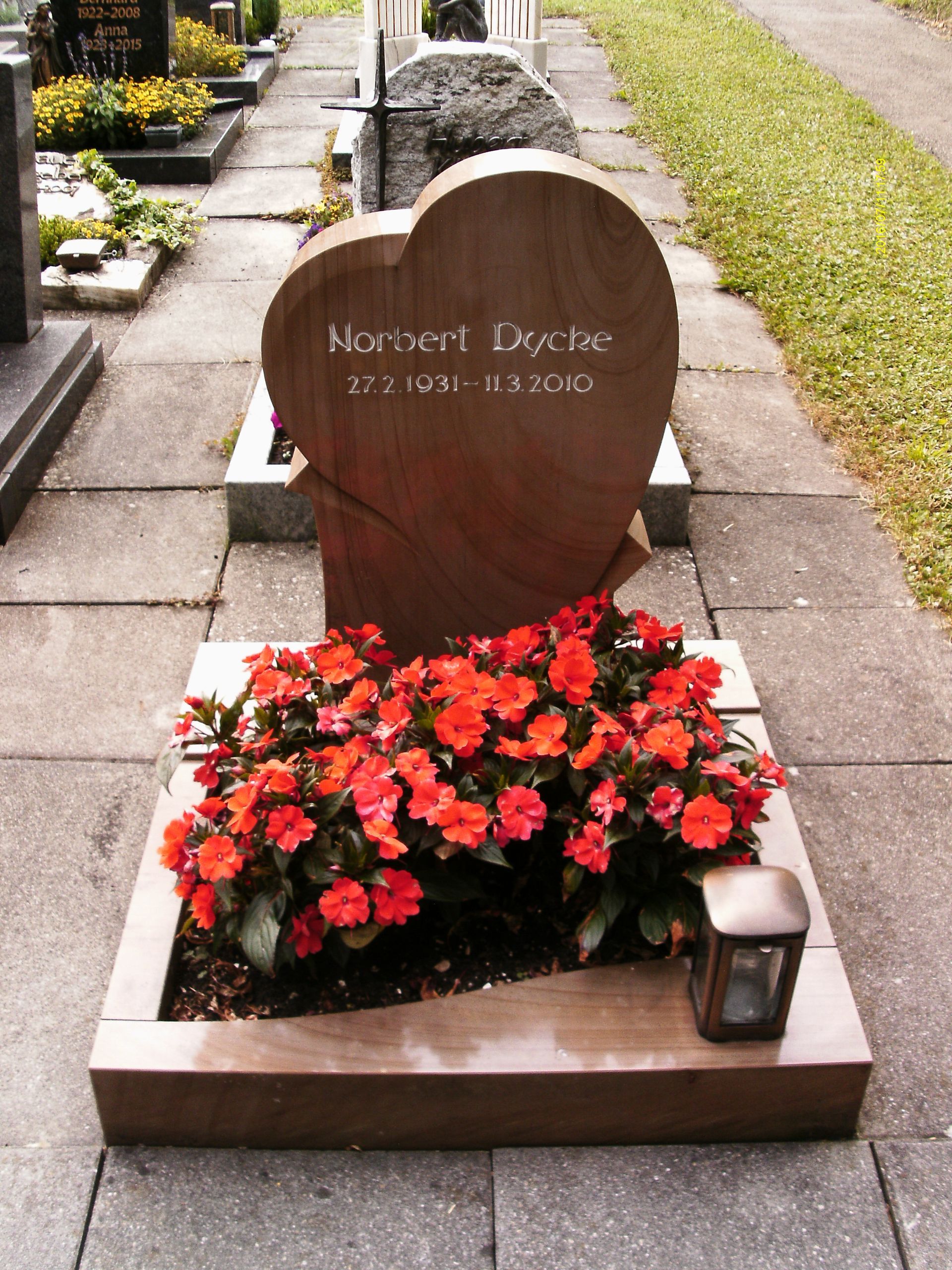Ein herzförmiger Grabstein auf einem Friedhof mit roten Blumen