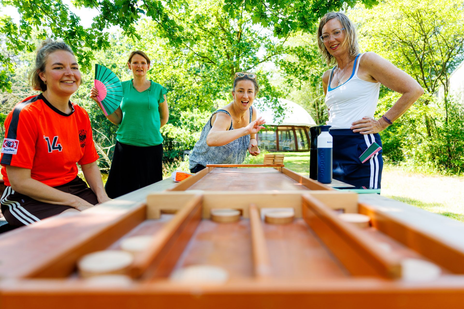 Eetkamer met lange houten tafels, witte stoelen en een groene muurschildering.