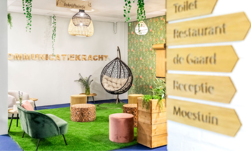 Loungegedeelte binnen met groen kunstgras, hangstoel en borden die de weg wijzen naar de faciliteiten.