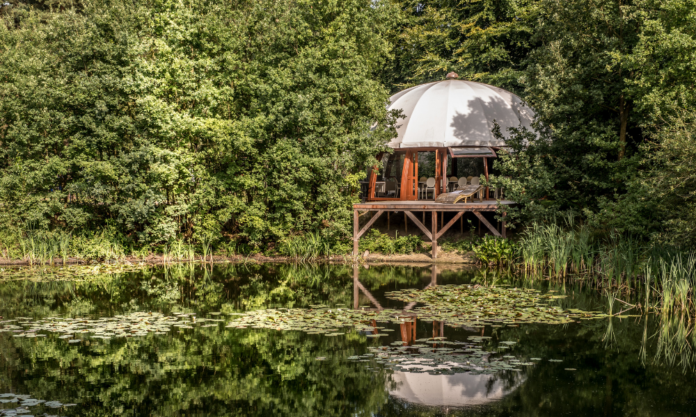 Een koepelvormige vergaderlocatie staat op een klein eiland in het midden van een meer, omgeven door bomen