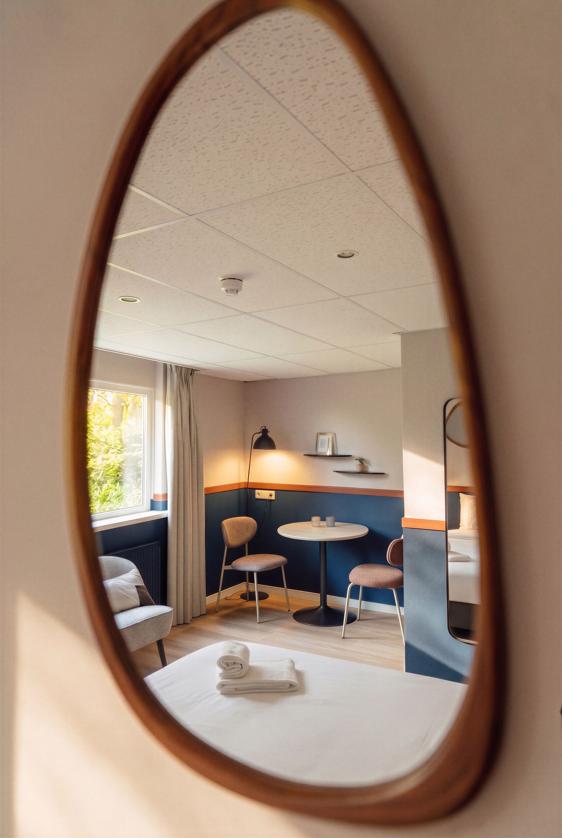 Bed met kussens, bloemen in een vaas en een gouden bijzettafel. Groengetinte muur, wit beddengoed en kleurrijke bloemen.
