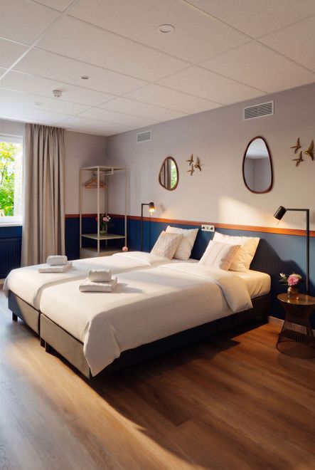 Vogelhuisje en bed met kussens met patronen tegen een lichtgroene muur, klein tafeltje met bloemen.