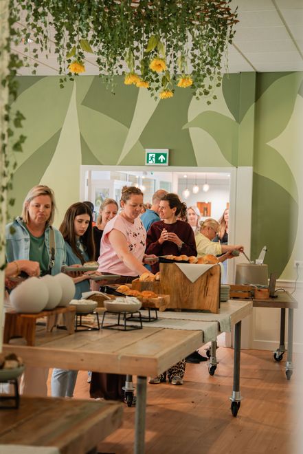Een lichte, luchtige kamer met houten balken en ramen, kleine tafels en banken met gele kussens.