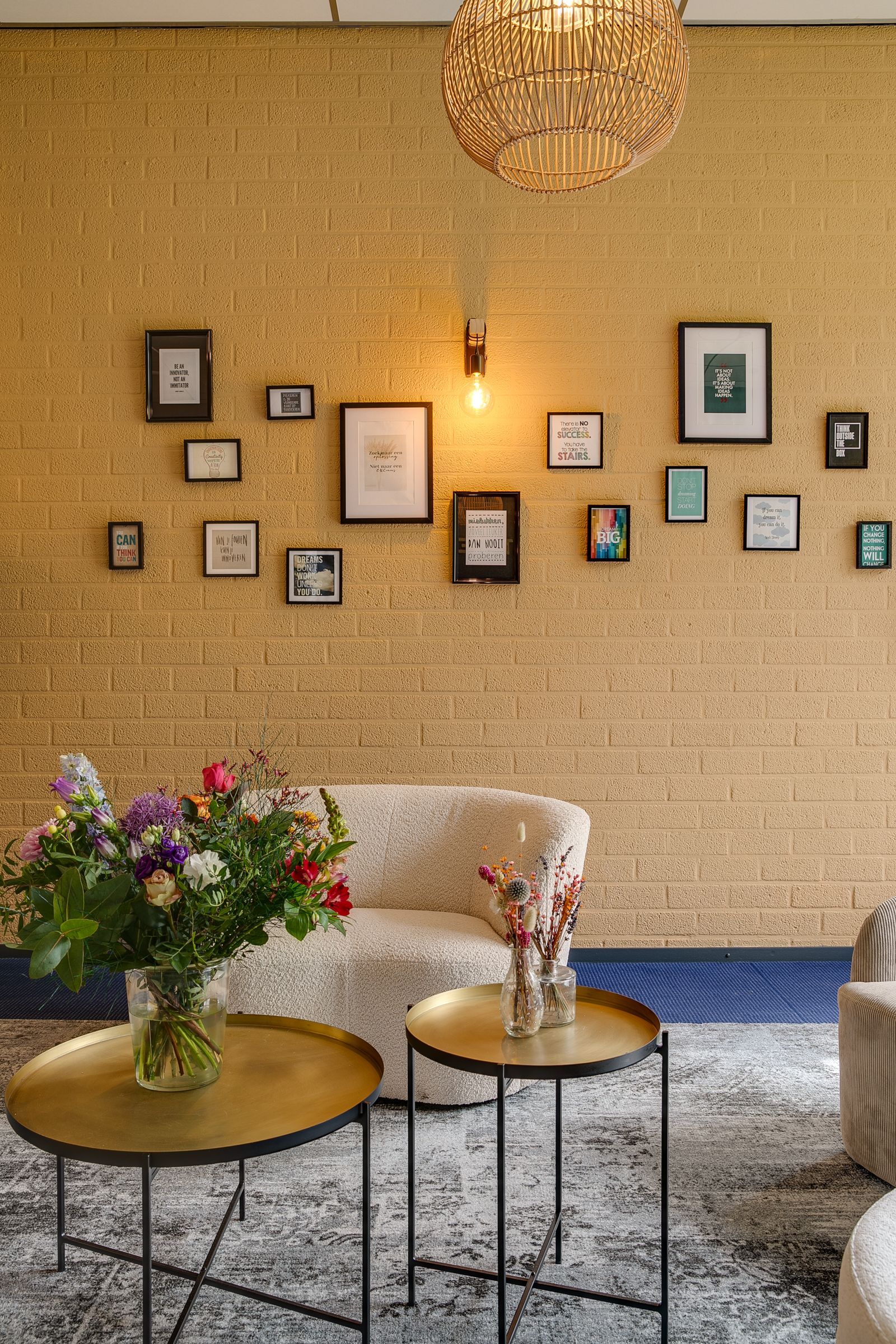 Woonkamer met een muur met goudkleurige textuur, ingelijste foto's, een bank, salontafels en een boeket bloemen.