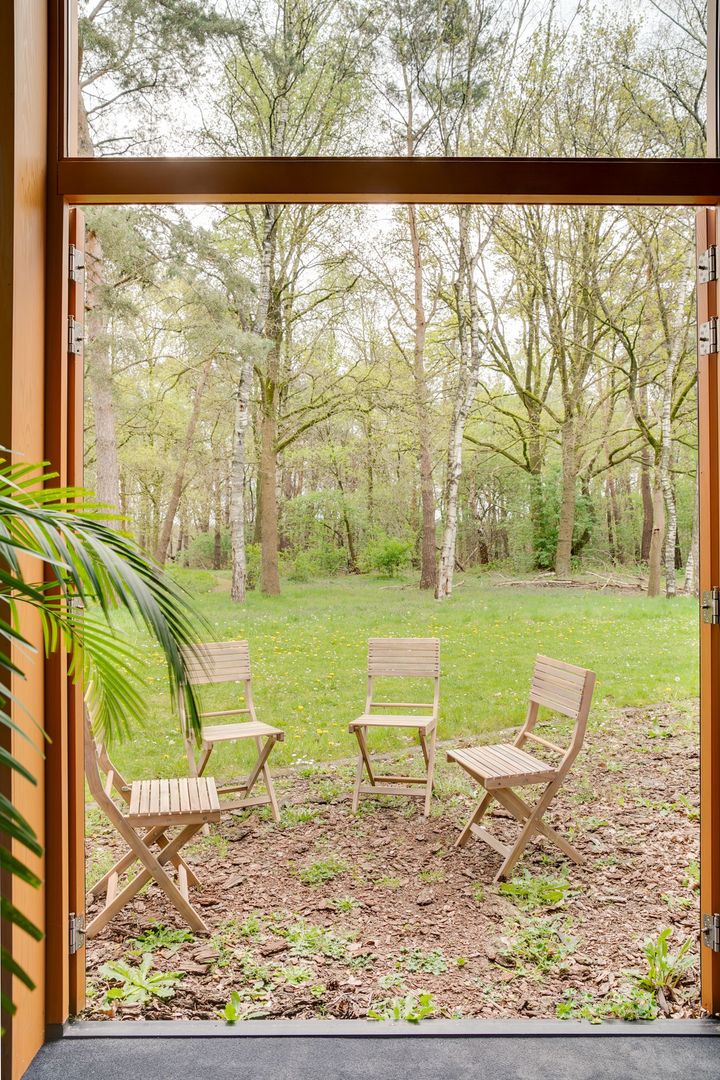 Houten stoelen op een grasveld, omlijst door een open houten deuropening met uitzicht op bomen en planten.