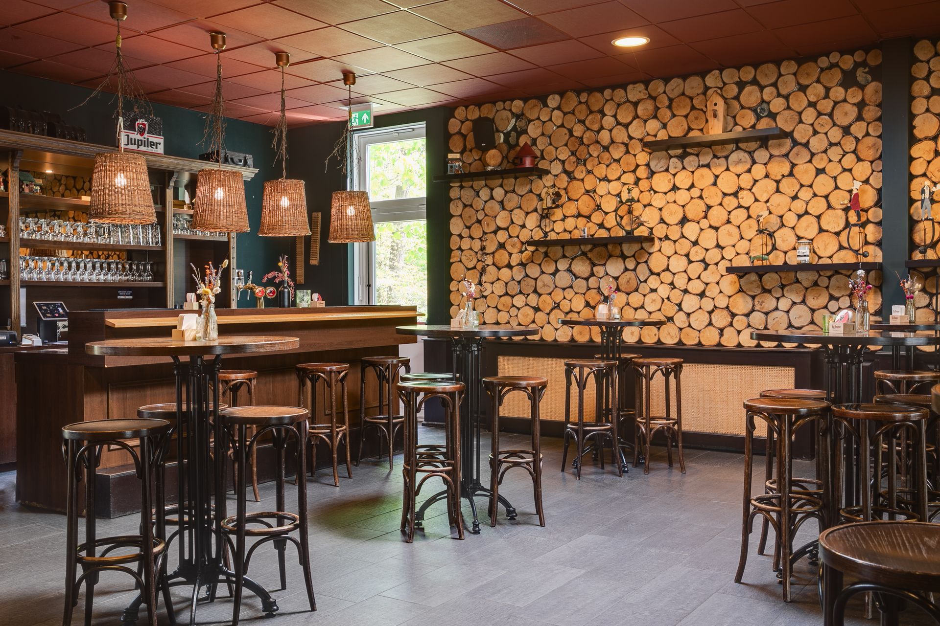 Interieur van een bar met houten wanden en tafels. Er staan ​​barkrukken opgesteld en er hangen lampen aan het plafond.