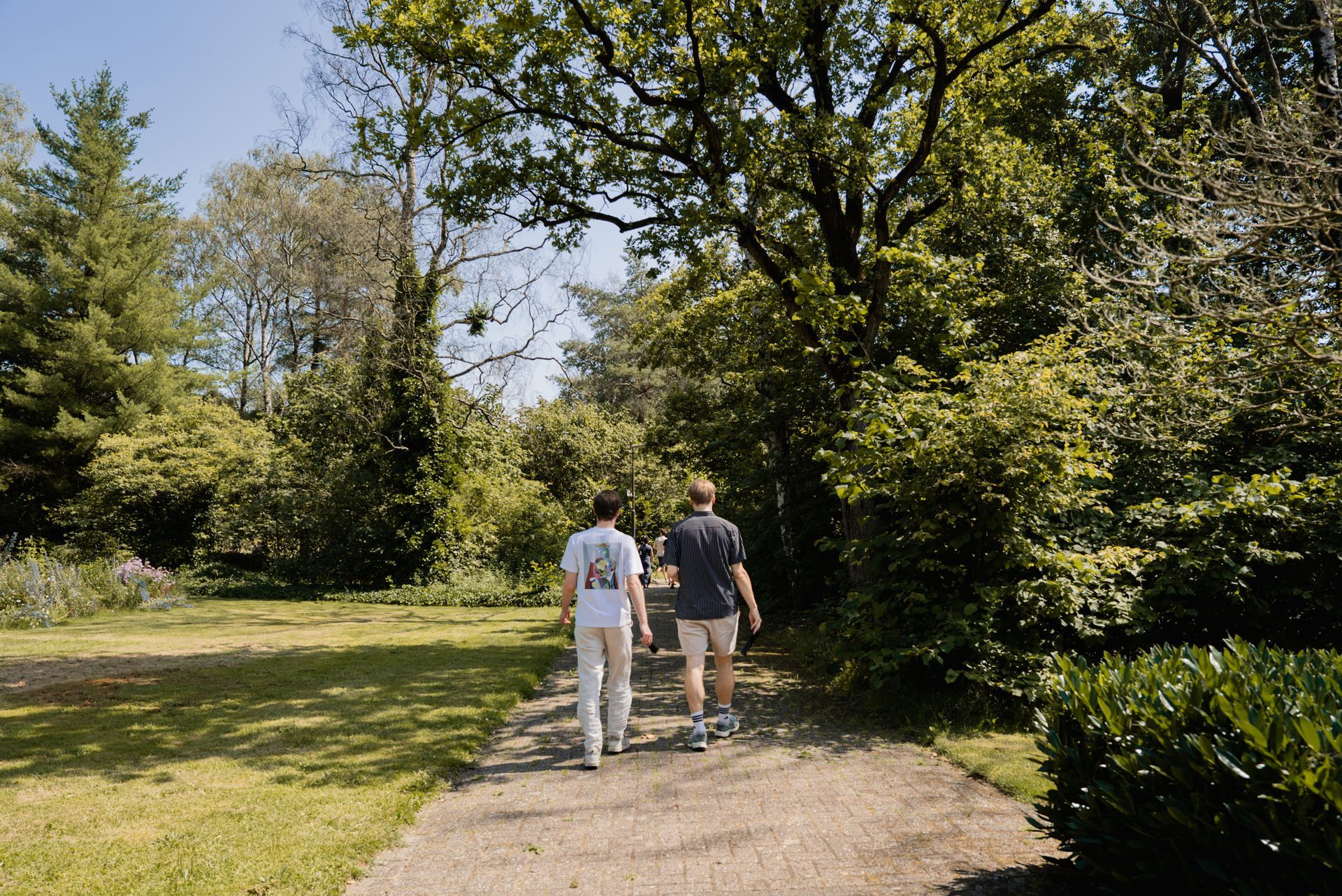 Klaslokaal met tafels, stoelen en grote ramen met uitzicht op een tuin. De muren zijn beschilderd met een boommotief en er is een houten deur.