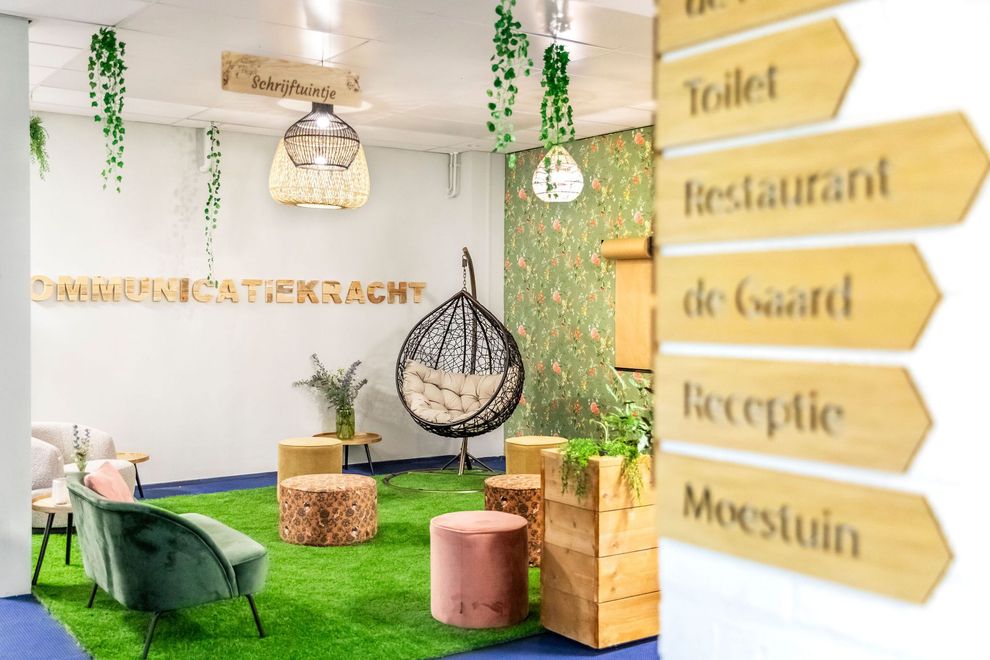 Ontspanningsruimte met groen, hanglampen, zitgelegenheid en houten borden die de richting aangeven.