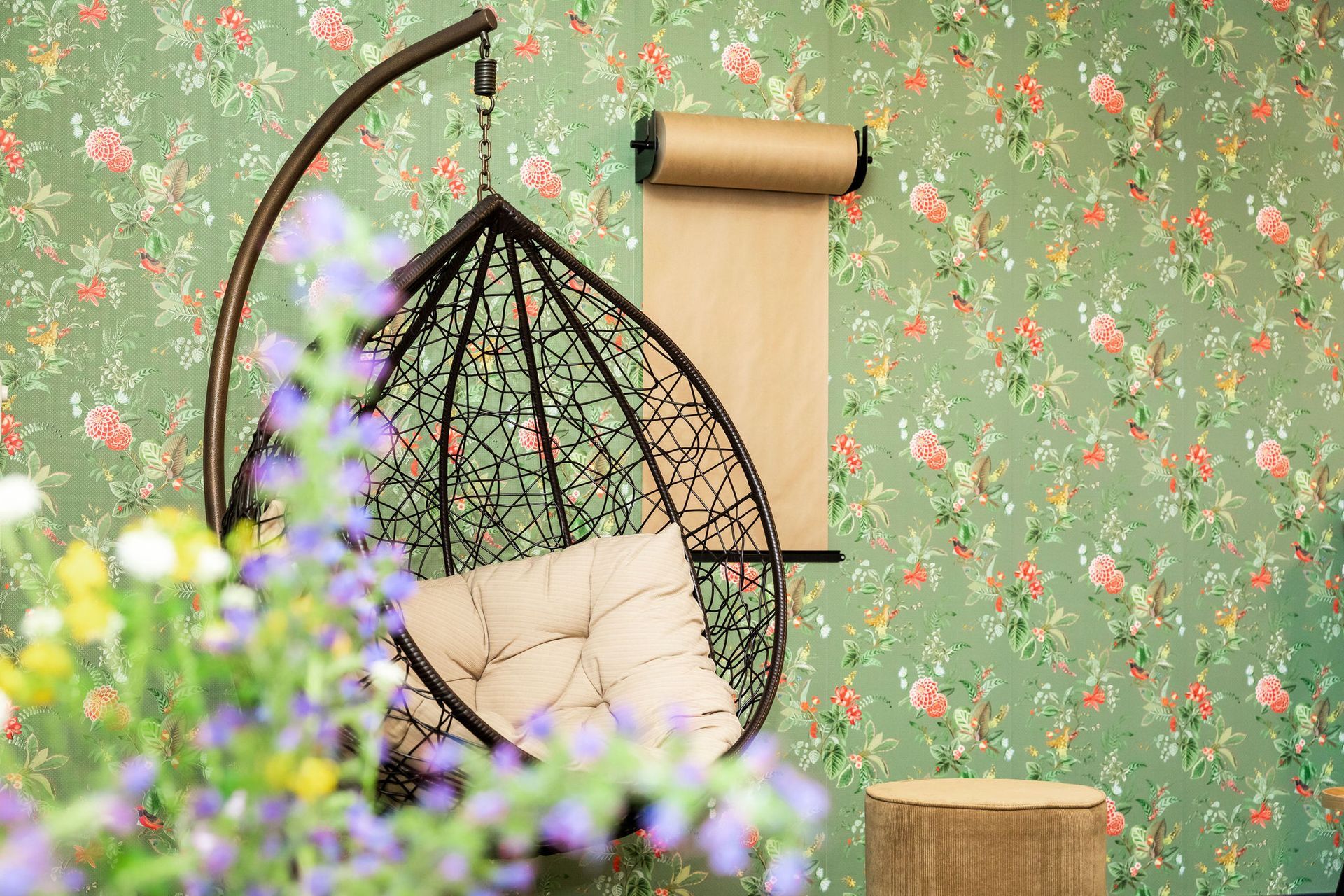 Een kas met glazen wanden in een bloementuin, met een houten schuttingpaal op de voorgrond.