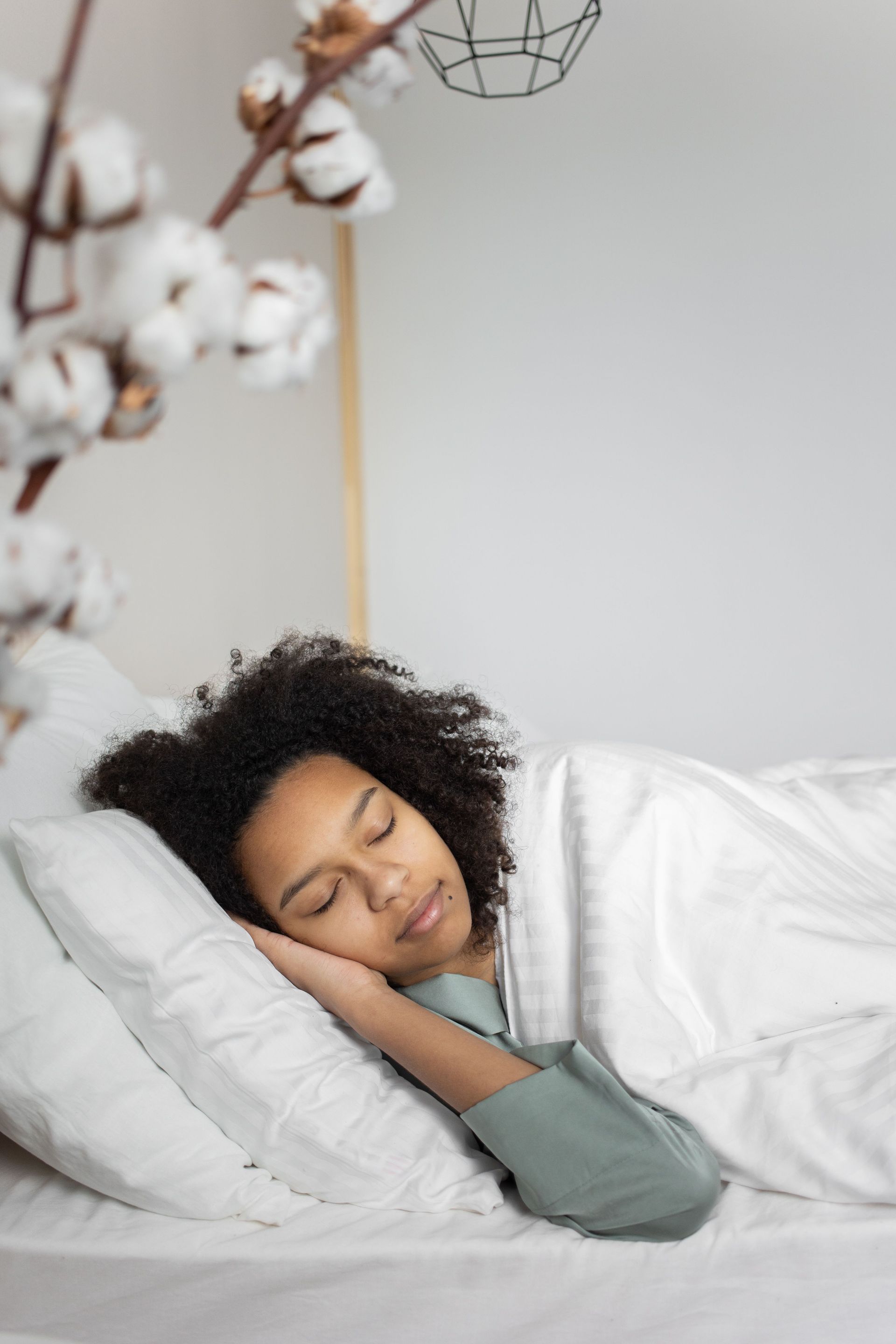 Slaapkamer met bureau bij het raam, bloemstuk en wit bed. Groene muren en een klein krukje.