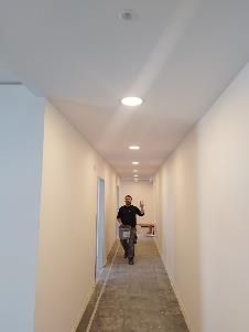 Eine Person mit einer Schleifmaschine in einem Flur; die Wände sind weiß.