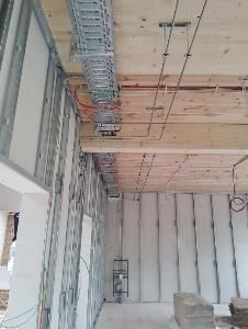 Innenansicht der Baustelle mit Metallrahmen, Verkabelung, Kabeltrassen und freiliegender Holzdecke.