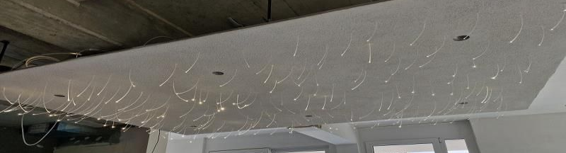 Eine rechteckige Deckenplatte mit vielen hängenden, leuchtenden Glasfaserlichtern.