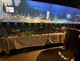 Buffet mit Speisen unter einer großen Leinwand, auf der eine Stadtszene gezeigt wird.