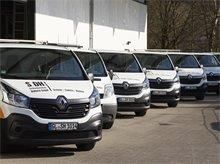 Eine Reihe weißer Renault-Transporter mit Firmenlogo parkt vor einem Gebäude.