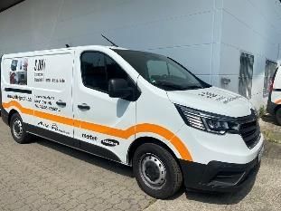 Ein weißer Lieferwagen mit orangefarbenen Akzenten parkt neben einem Gebäude. Der Wagen ist mit Firmenlogos und -schriftzügen versehen.