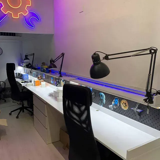 Una habitación con un escritorio largo y sillas y un letrero de neón en la pared.