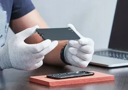 Un hombre que lleva guantes blancos sostiene un teléfono celular en sus manos.