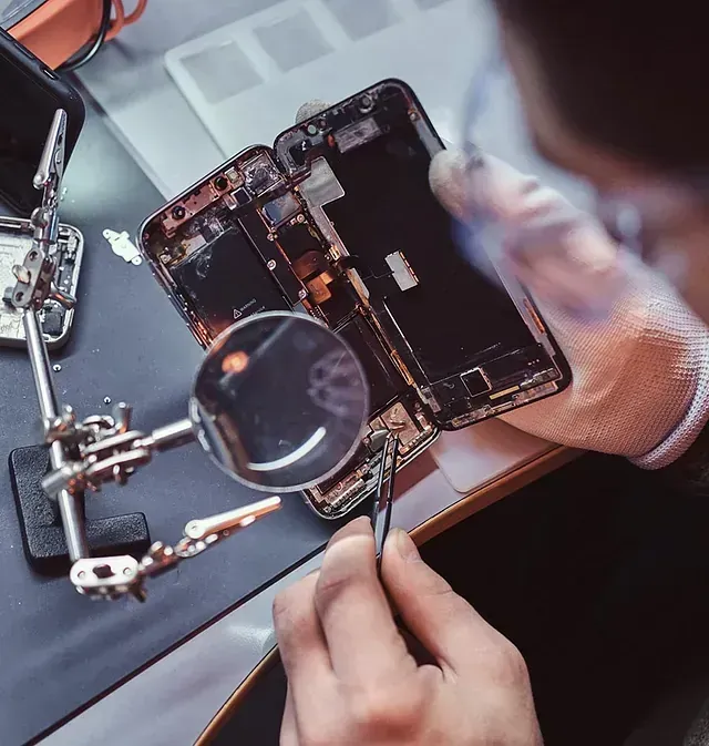 Un hombre está reparando un teléfono celular con una lupa.