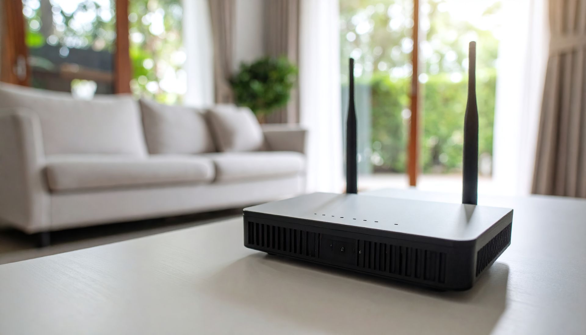Un routeur internet sans fil noir est posé sur une table blanche dans un salon moderne et lumineux.