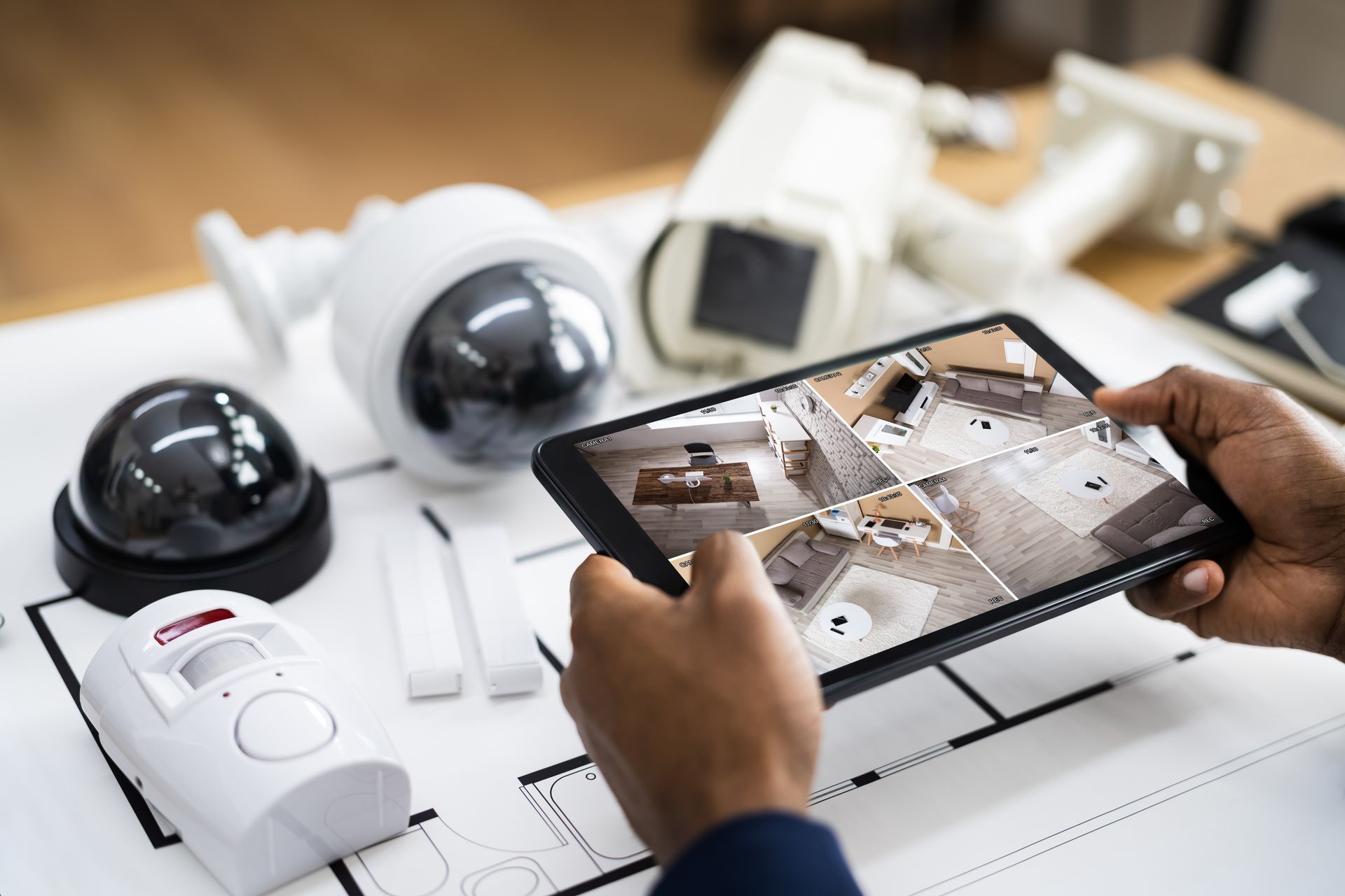 Des mains tiennent une tablette affichant le flux vidéo de quatre caméras de sécurité.