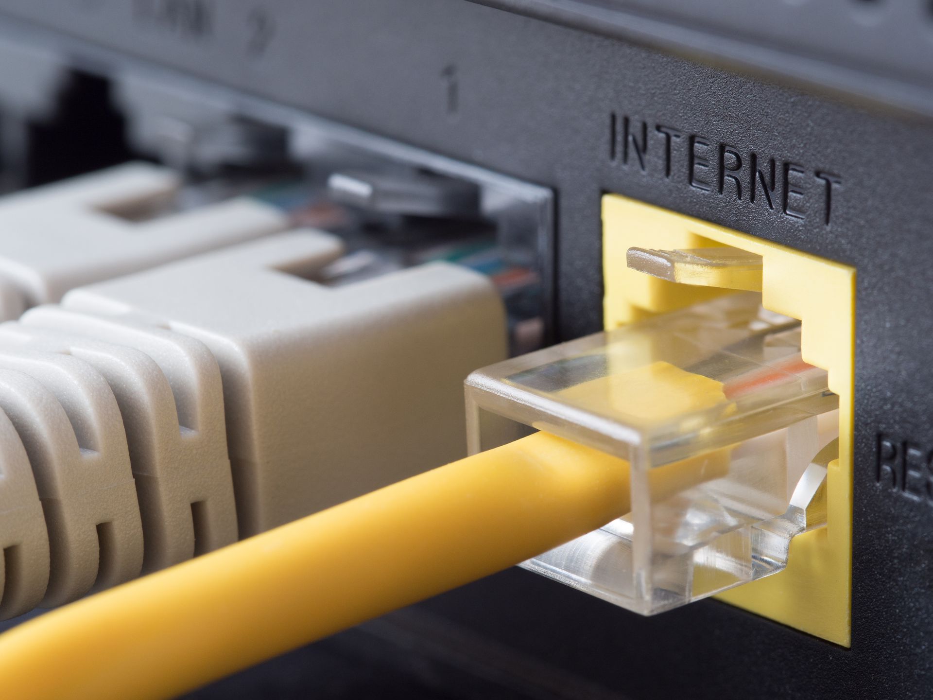 Un câble Ethernet jaune branché sur le port jaune INTERNET d'un routeur réseau, à côté d'autres câbles gris.