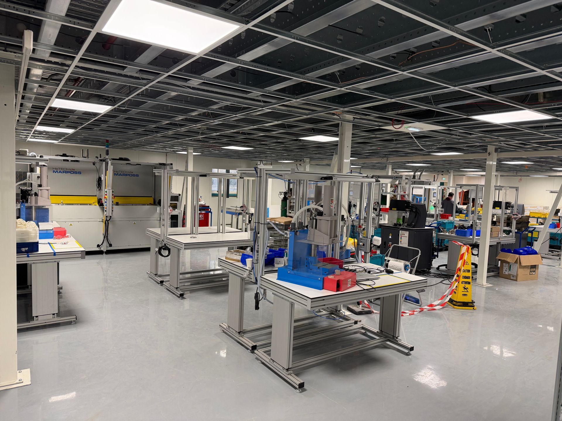 Un atelier de fabrication lumineux comprenant plusieurs postes de travail avec des structures métalliques, des équipements et des composants bleus.