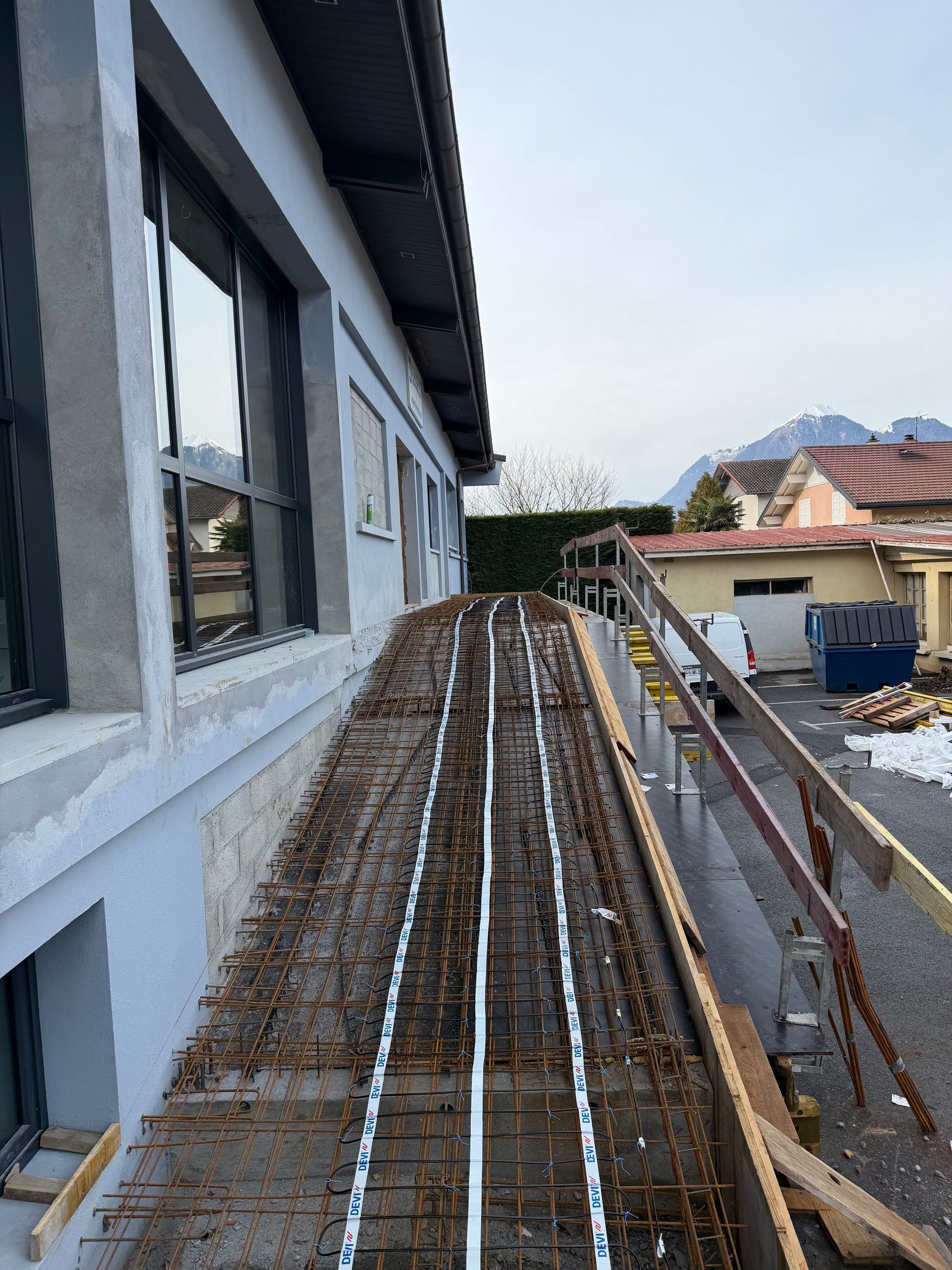Un chantier de construction montrant une rampe en cours d'aménagement, avec une armature métallique et des conduits blancs en surface.