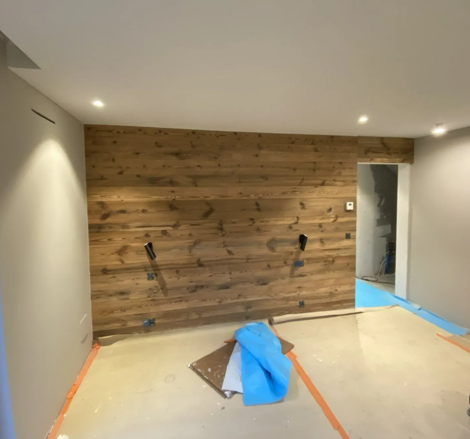 Une pièce en cours de rénovation avec un mur lambrissé rustique, des murs peints dans des tons neutres, un éclairage encastré et un revêtement de sol.