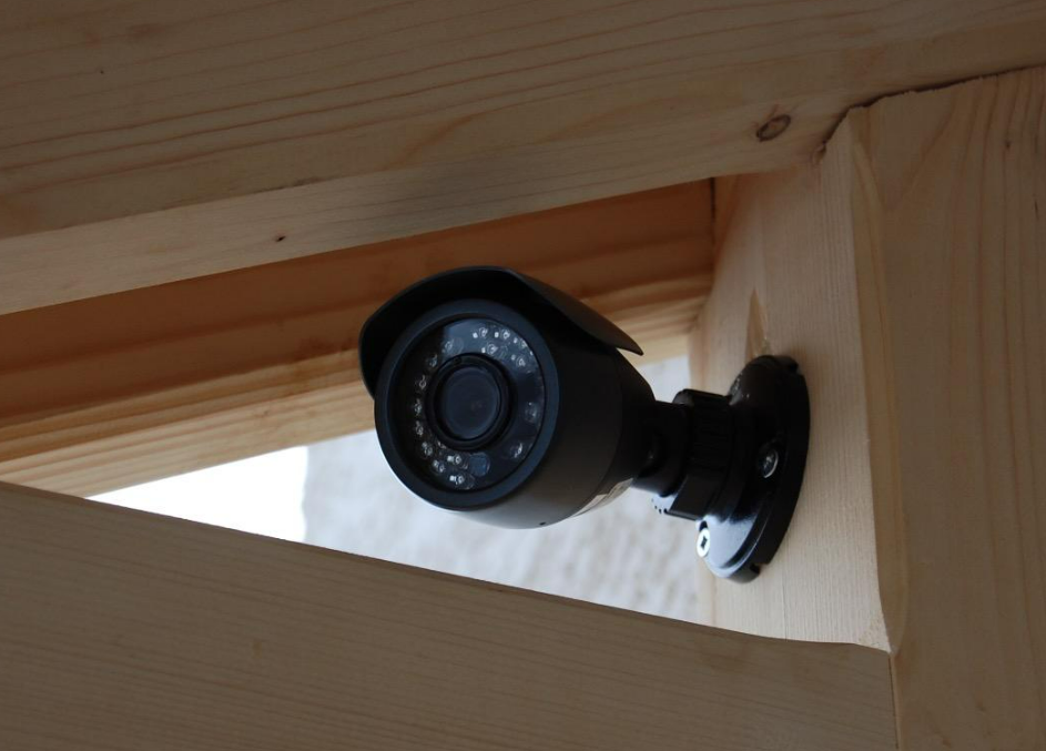 Une caméra de sécurité noire de type balle, montée sur une poutre en bois dans la structure d'un bâtiment.