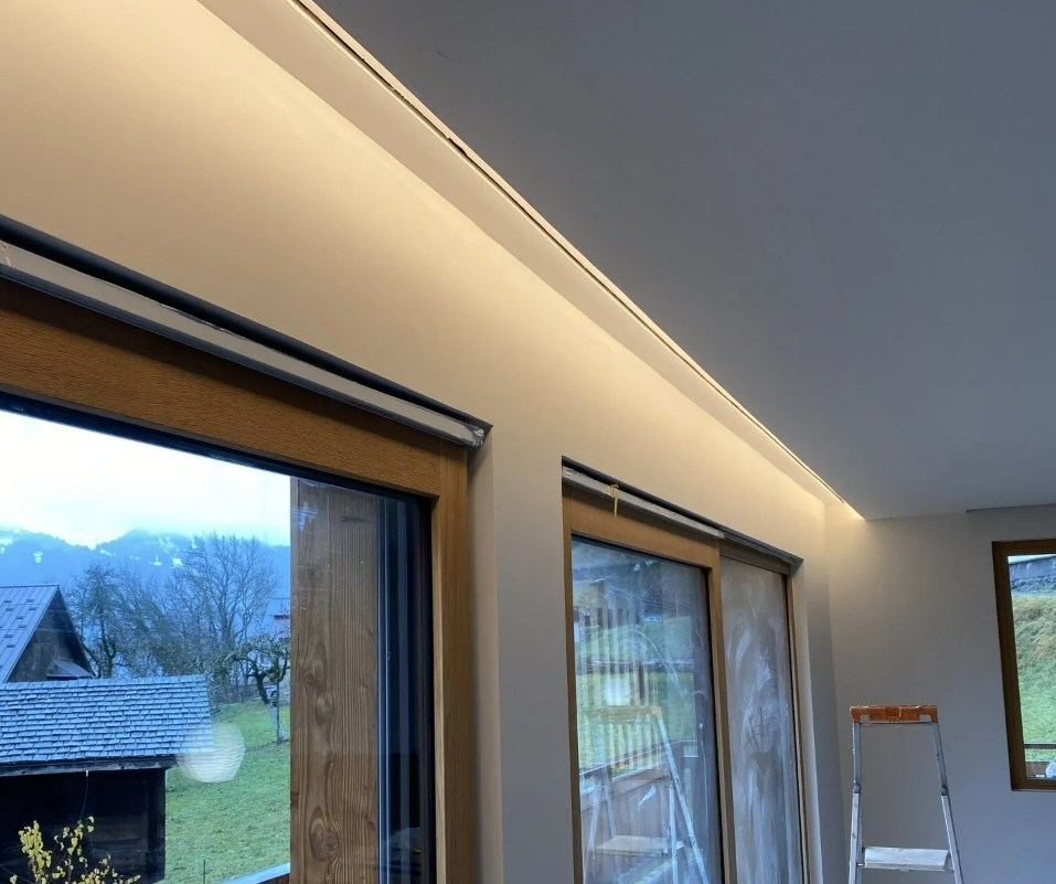 Vue en contre-plongée d'un intérieur moderne avec éclairage à LED encastré au plafond au-dessus de grandes fenêtres donnant sur un paysage rural.