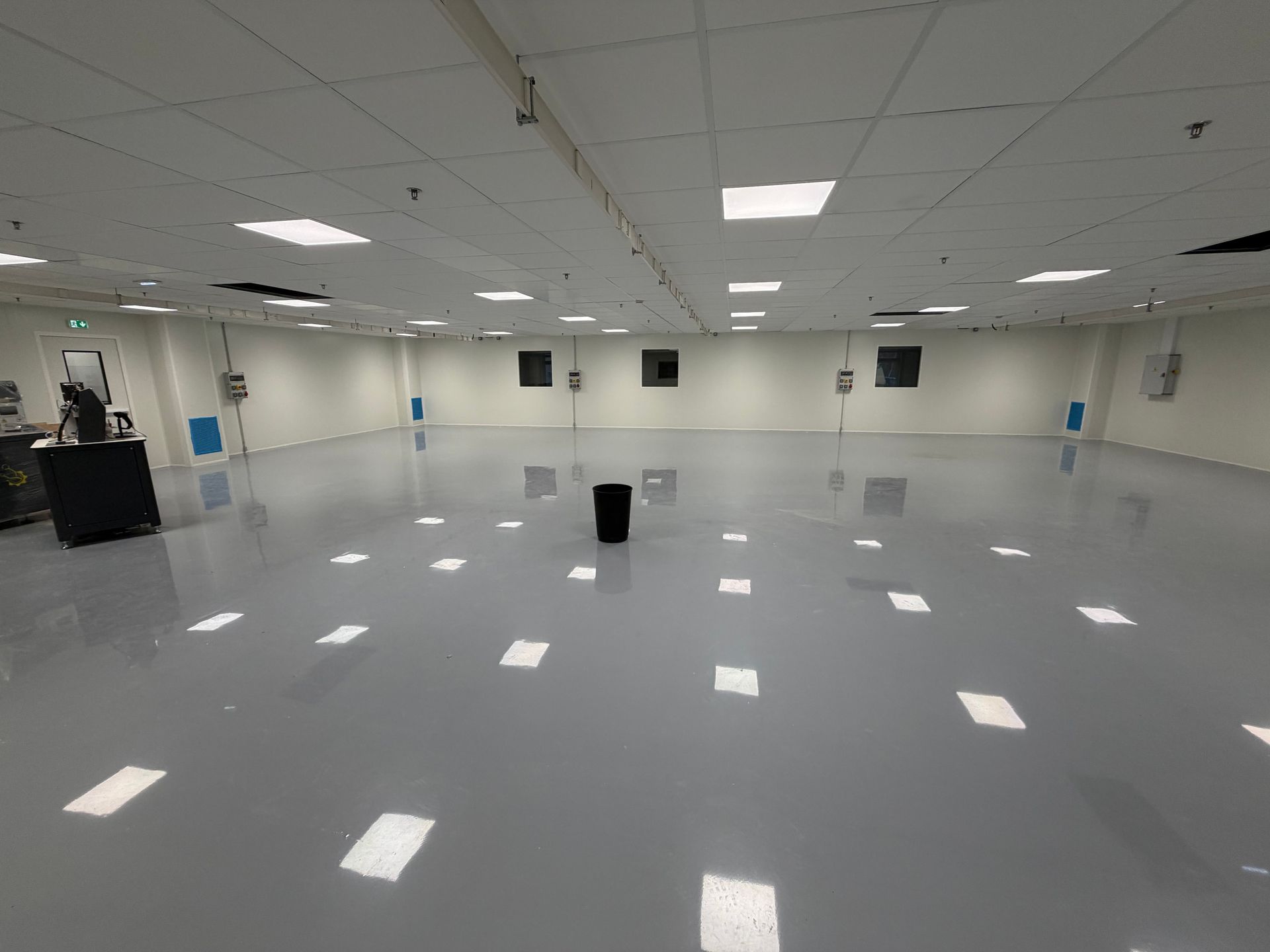 Vue grand angle d'une grande pièce industrielle vide, de couleur gris clair, avec un sol brillant et des spots encastrés au plafond.