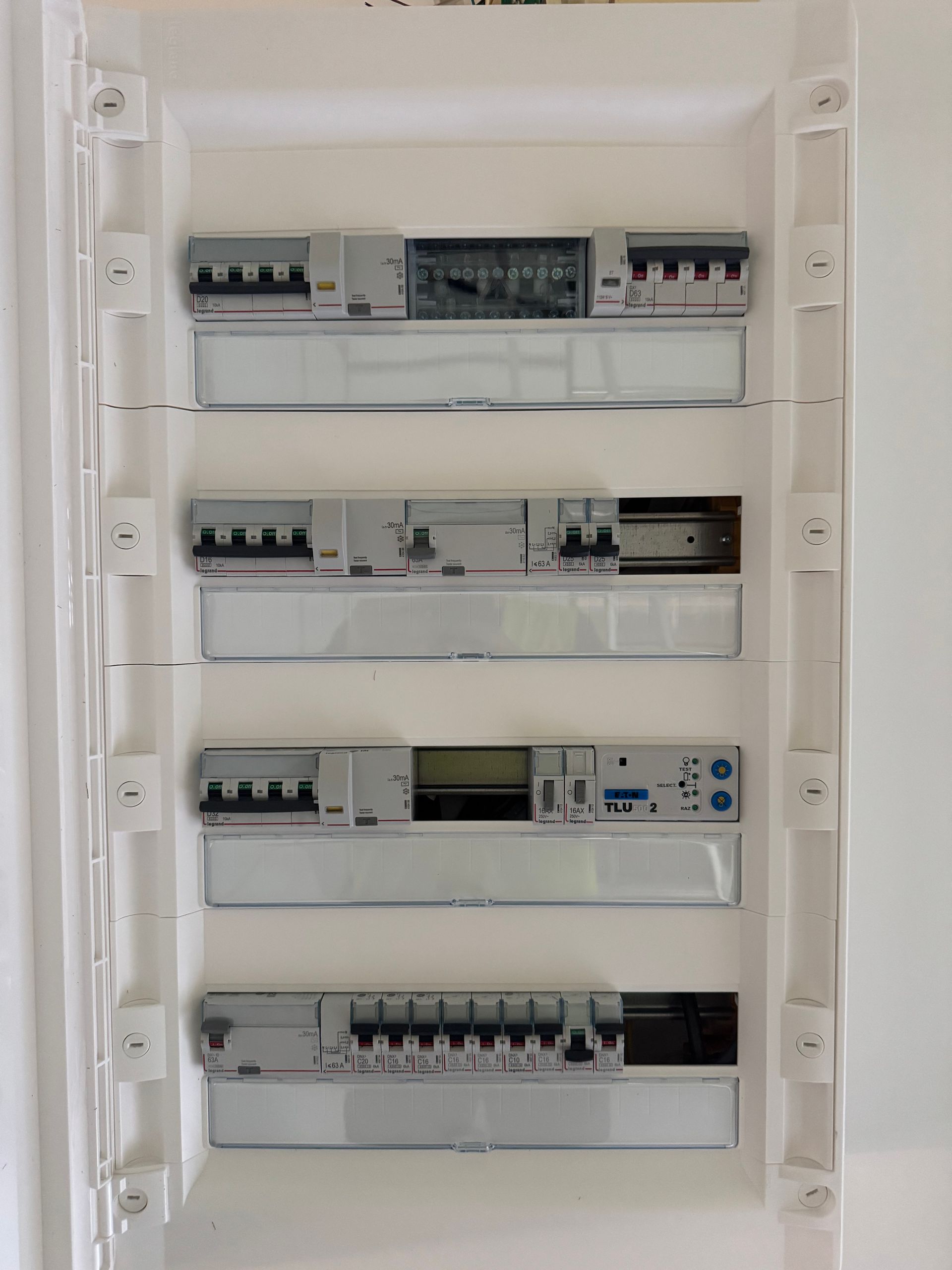 Un tableau électrique mural à quatre rangées, dont certaines contiennent des disjoncteurs et des composants modulaires.