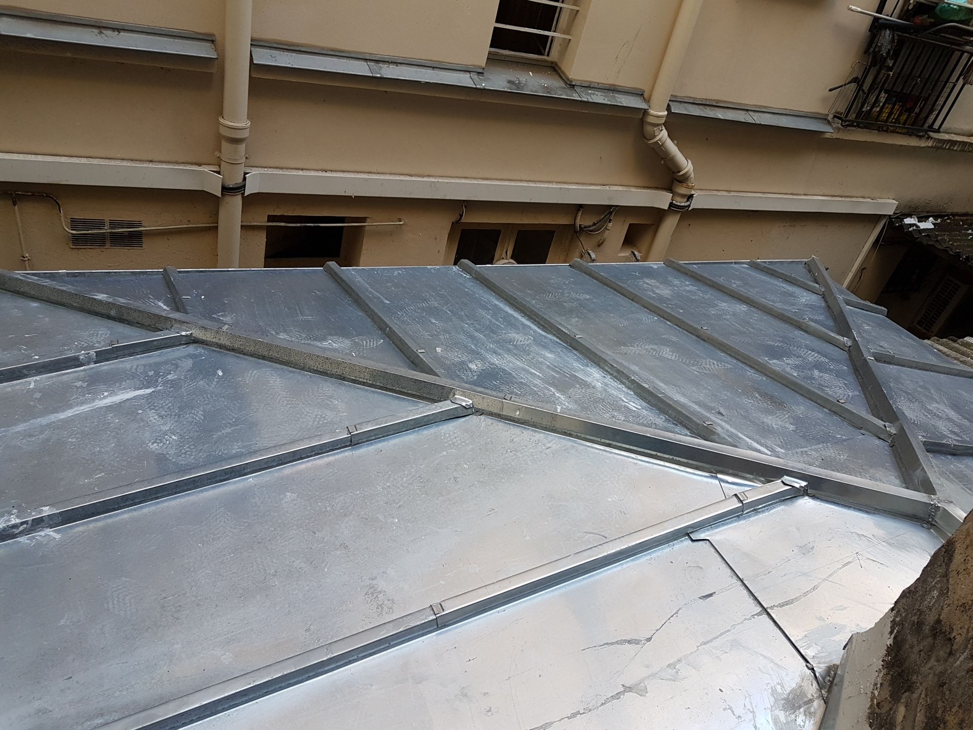 Gouttière et descente pluviale au coin d'une maison, sur fond de ciel bleu.