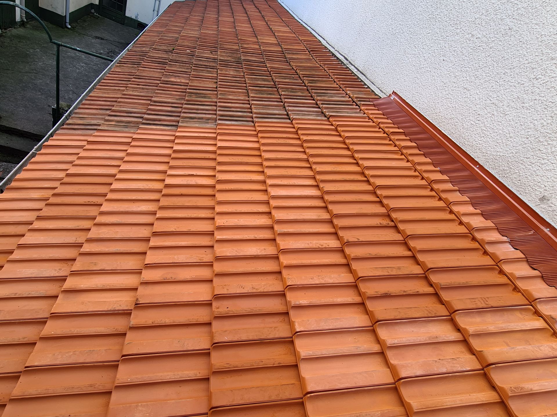 Un ouvrier rénove un toit de tuiles rouges.