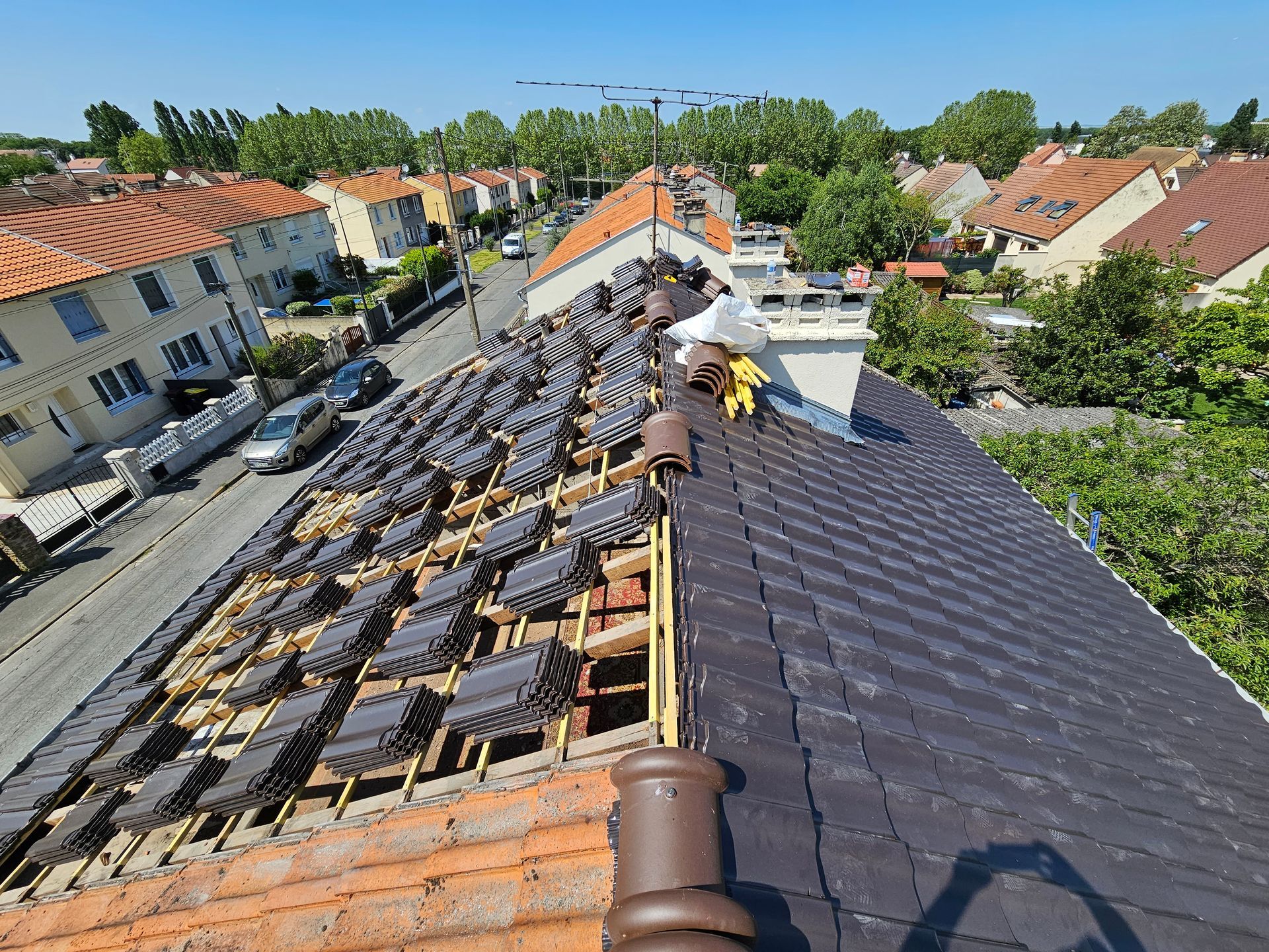 Un ouvrier ganté pose des bardeaux sur un toit, un marteau étant visible en arrière-plan.