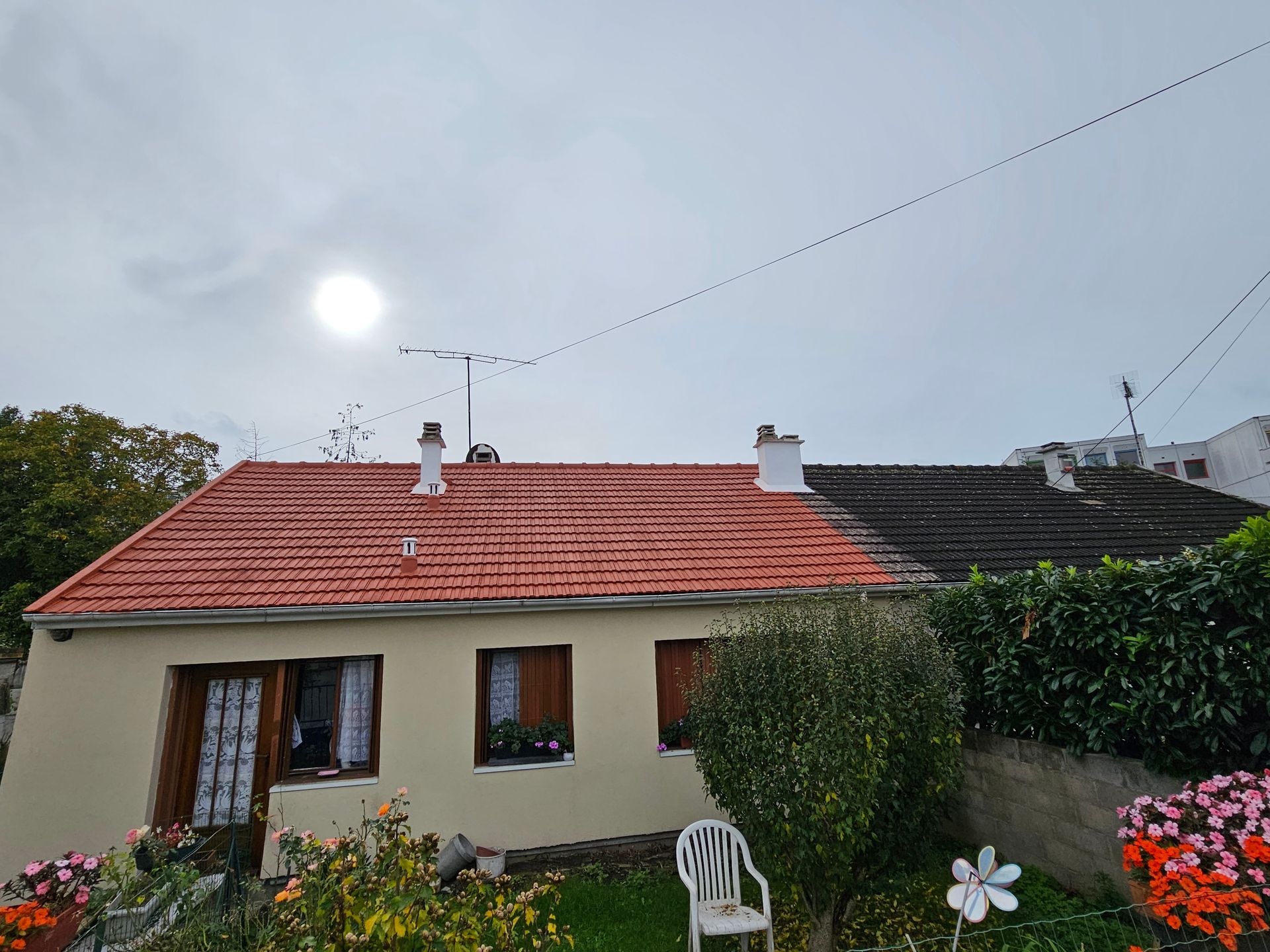 Façade d'une maison en stuc au toit de tuiles rouges se détachant sur un ciel bleu nuageux.