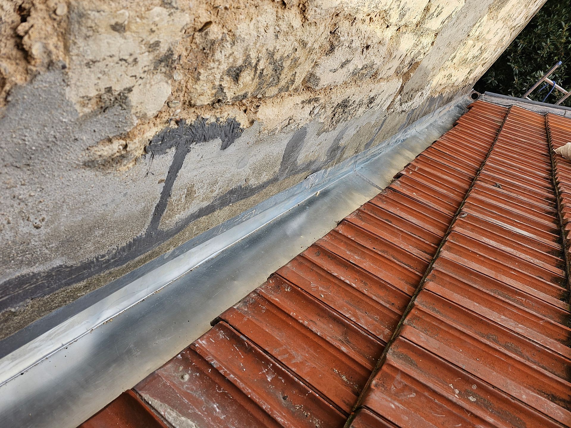 Gros plan sur le toit et la gouttière d'une maison avec une descente pluviale blanche.