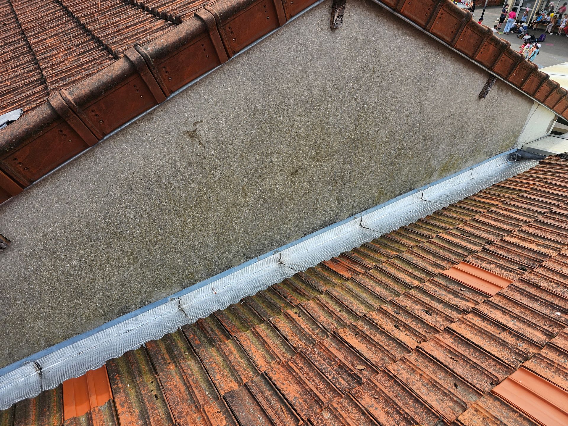 Toiture extérieure d'une maison avec gouttières blanches et bardeaux gris, centrée sur une descente pluviale.