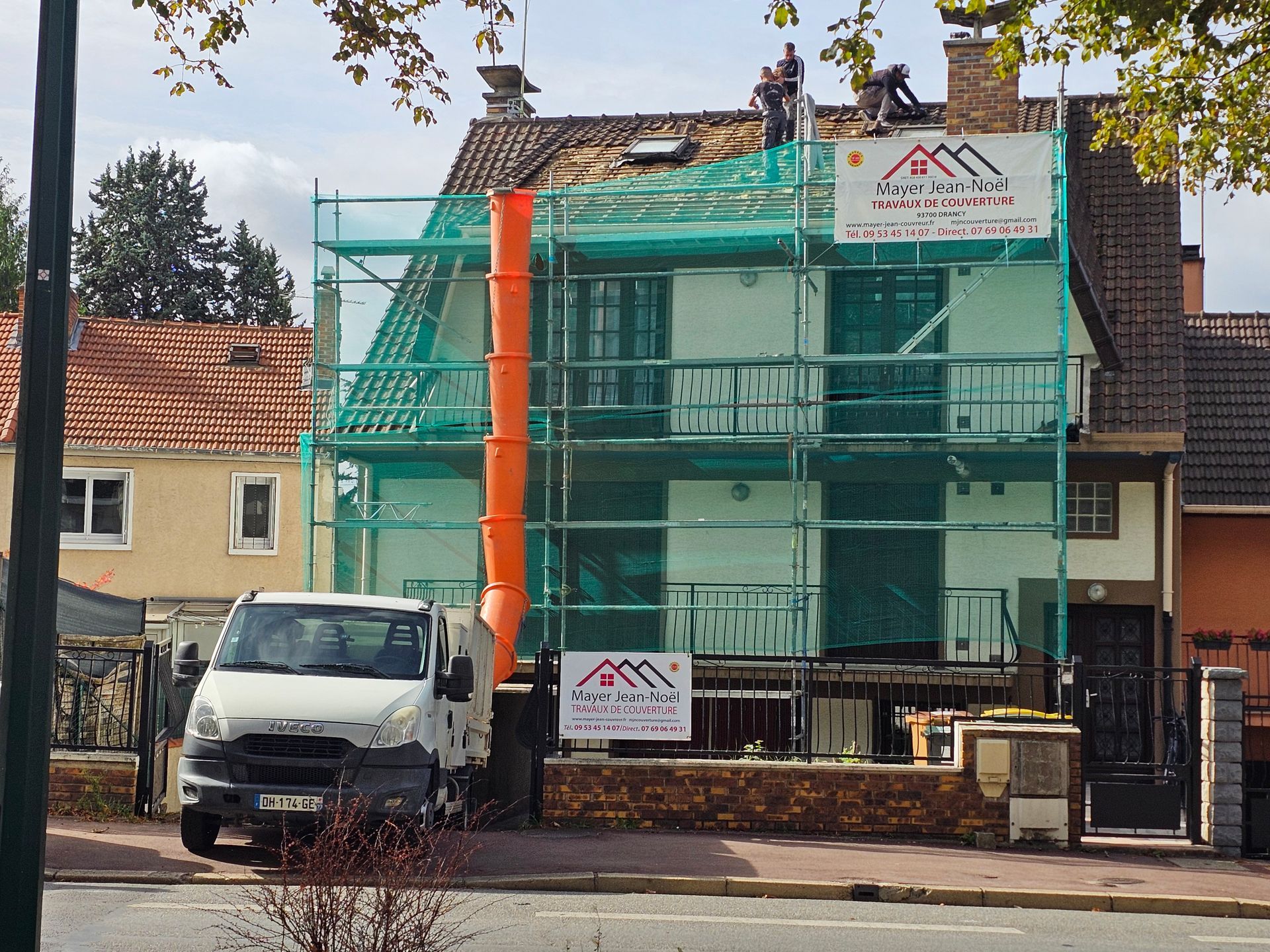 Un ouvrier avec un harnais nettoie un toit en tuiles à l'aide d'un nettoyeur haute pression.