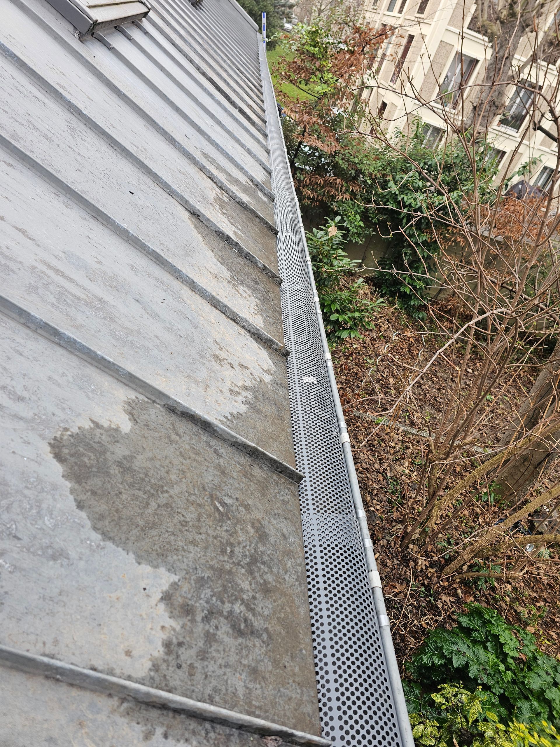 Avant-toit d'une maison blanche avec toit de tuiles grises et gouttières.