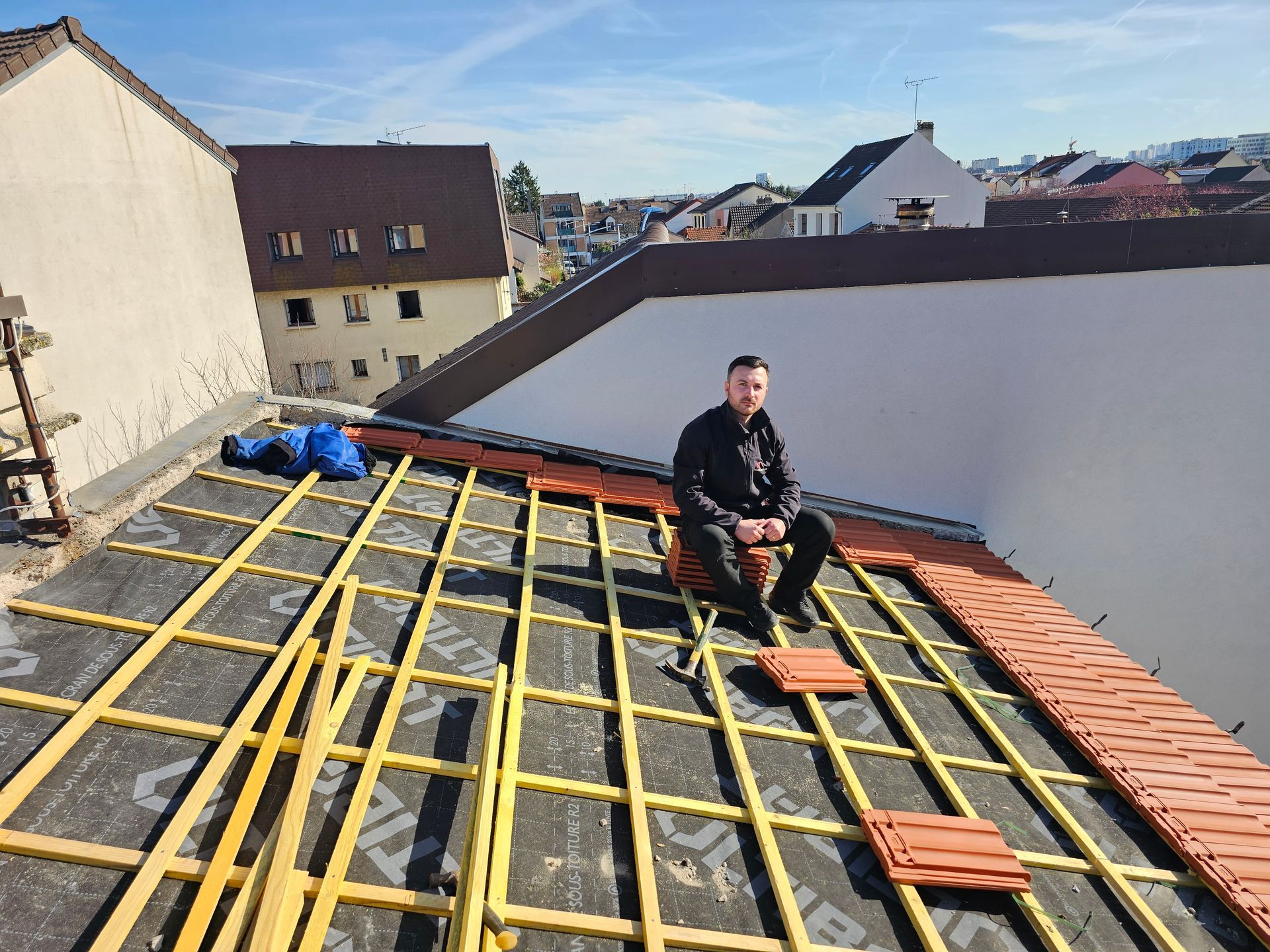 Petite maison au toit de tuiles rouges, aux murs beiges et avec une fenêtre donnant sur un ciel nuageux.